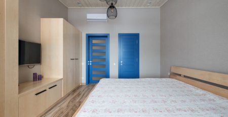 Спалня със светли мебели и две интериорни сини врати